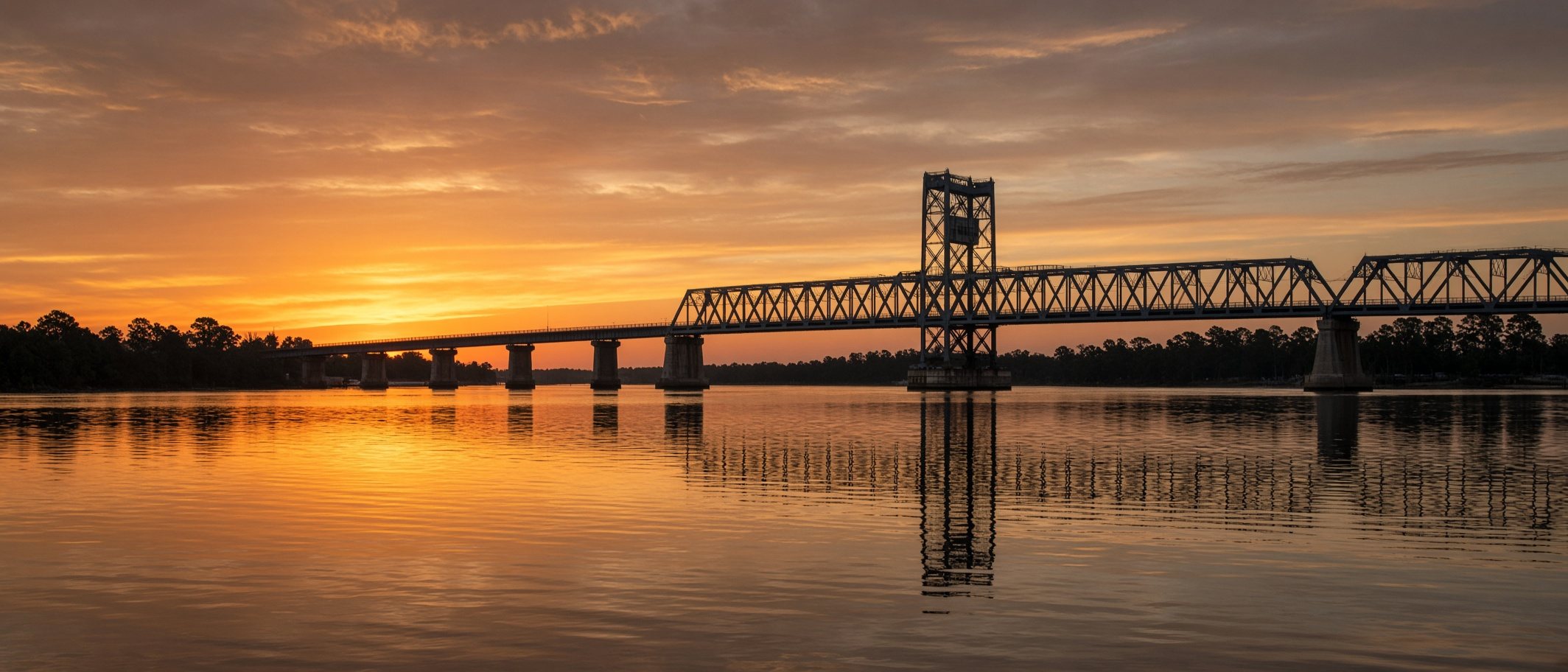 A steel bridge over a wide river at sunset